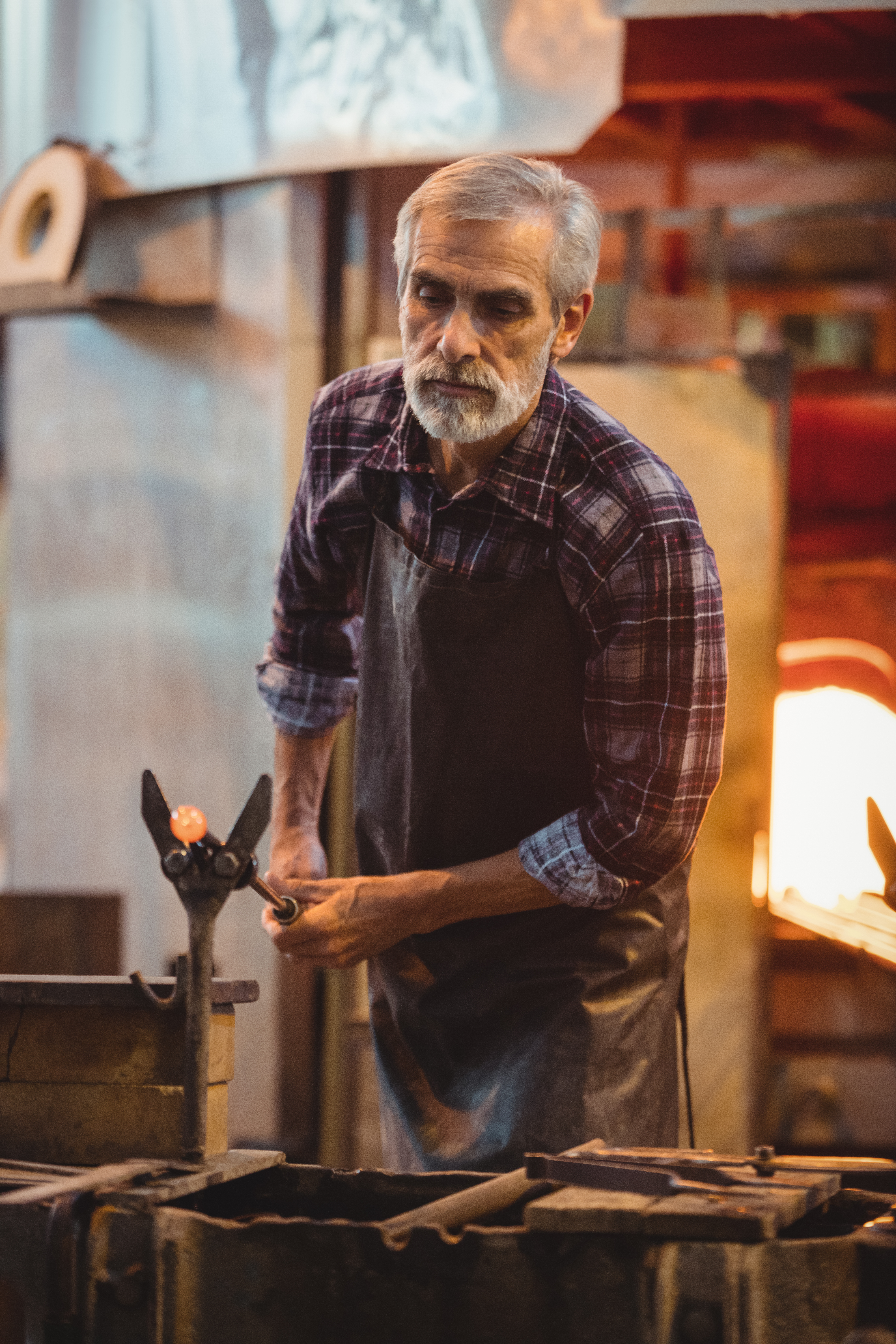 Glassblower shaping a molten glass at glassblowing factory